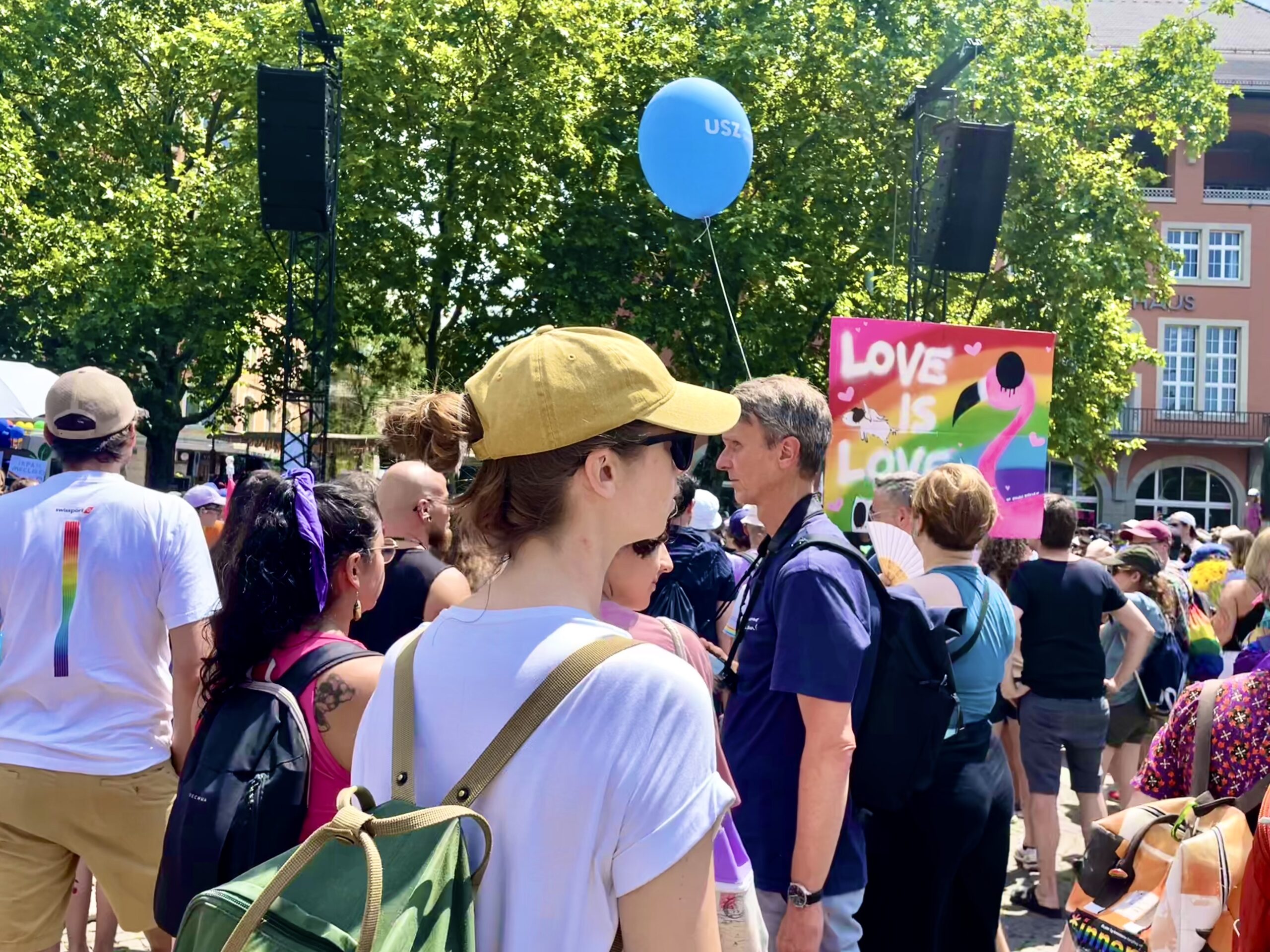 A crowd at Zurich Pride in 2025 beneath a Love is Love sign